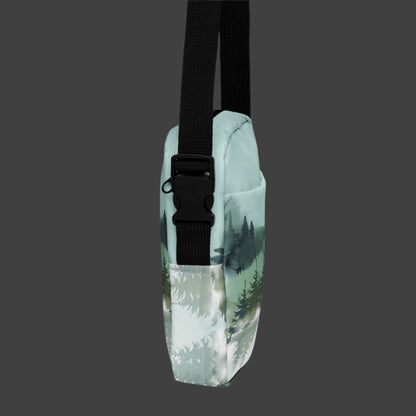 Image: Winter Forest Small Cross Body Bag. This nature inspired sling bag has an ombre snowy mountain print that fades from a blue gray sky to mountains and pine trees to white snow. This mini backpack has a zipper closure and two storage pockets for hands free outdoor adventures. Great for tween girls, teens and ladies, by jaecrece