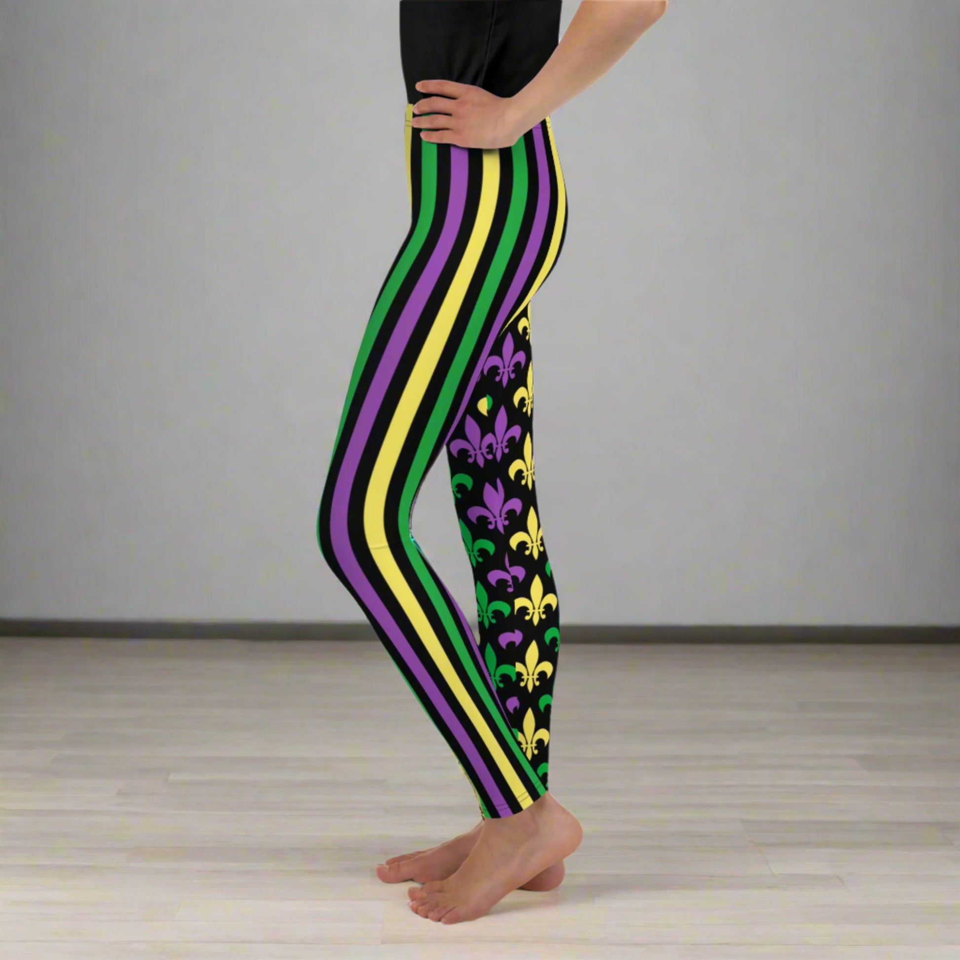 Alt text: "Mardi Gras Stripes and Fleur de Lis Youth Leggings, size 8-20. Black leggings with a fleur de lis pattern on one leg and bright green, purple, and yellow stripes on the other. Elastic, soft, and durable with vibrant colors. Part of a matching collection for younger children and women, each pair is precision-cut and hand-sewn for a perfect fit."