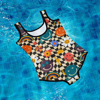 Smiley Face Checkerboard Girls One Piece Bathing Suit. This cute youth, teen or tween sized swimming suit features a black and khaki checkerboard background, with smiley face, rainbow and daisy graphics. It is perfect for vacation trips to the beach or pool. Family matching options available. By jaecrece.com