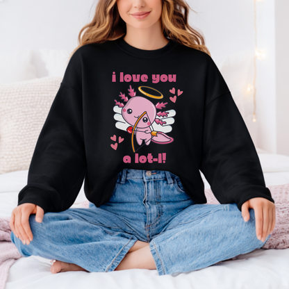 A woman sitting cross-legged on a bed wearing a black crewneck sweatshirt with a pink cartoon cupid graphic and the text 'i love you a lot-!!' in pink, paired with light blue jeans. Cute Valentine axolotl sweatshirt featuring an adorable cupid axolotl and playful I love you a lotl design. Cozy unisex crewneck pullover for Valentine’s Day celebrations, animal lovers, classroom parties, and everyday winter outfits.