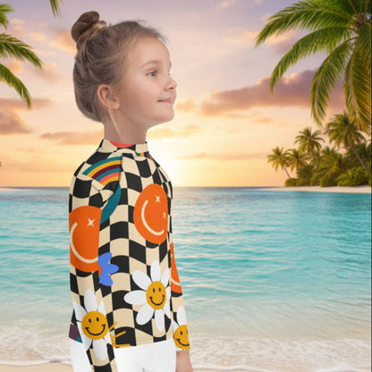Lifestyle photo of a tween girl on vacation wearing a colorful UPF 50+ rash guard with a retro wavy checkerboard design, daisies, stars, and cheerful smiley faces.