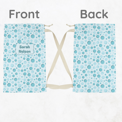 Front and back views of an aqua bubble print drawstring laundry bag, displayed side by side to show the colorful pattern, fabric construction, and plain cream drawstrings. This reusable laundry bag is a fun, practical choice for kids, tweens, and teens packing for summer camp, sleepovers, dorm life, and travel.