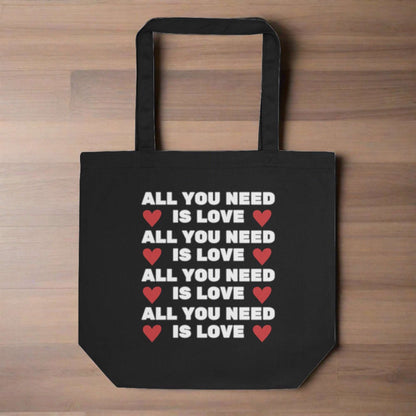 black tote bag that reads All You Need is Love, on a wooden background