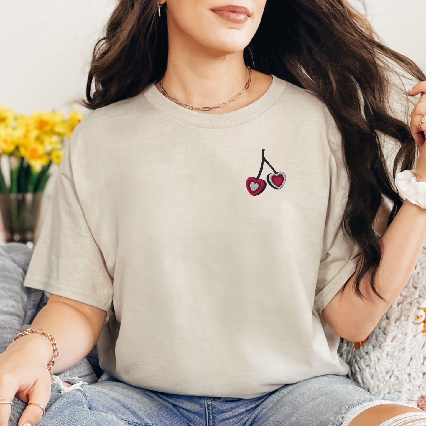 Woman wearing sand colored embroidered cherry hearts t shirt featuring soft red cherry heart embroidery on the front. This relaxed fit Gildan S5000 tee offers a neutral and timeless look perfect for casual everyday outfits, travel, and laid back styling. Matching girls shirt available separately for mommy and me outfits, creating coordinated family fashion with a soft minimal aesthetic.