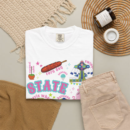 A nostalgic summer fair graphic on a T shirt features bold STATE FAIR lettering surrounded by a Ferris wheel, roller coaster, carnival swing ride, cotton candy, corn dogs, funnel cake, balloons, livestock, blue ribbon and ticket illustrations with colorful stars for a colorful fair day. The design blends carnival fun with classic Americana.