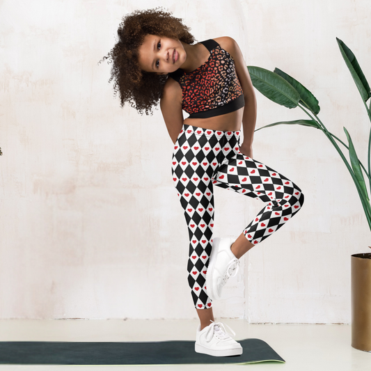 Black and white girls leggings feature a repeating harlequin diamond pattern decorated with bright red hearts. The playful design has a whimsical look that works for everyday outfits, Valentine's Day clothing, or a Queen of Hearts inspired costume. The full length leggings have a high waisted fit and soft stretchy fabric designed for comfortable movement during school, play, or lounging.