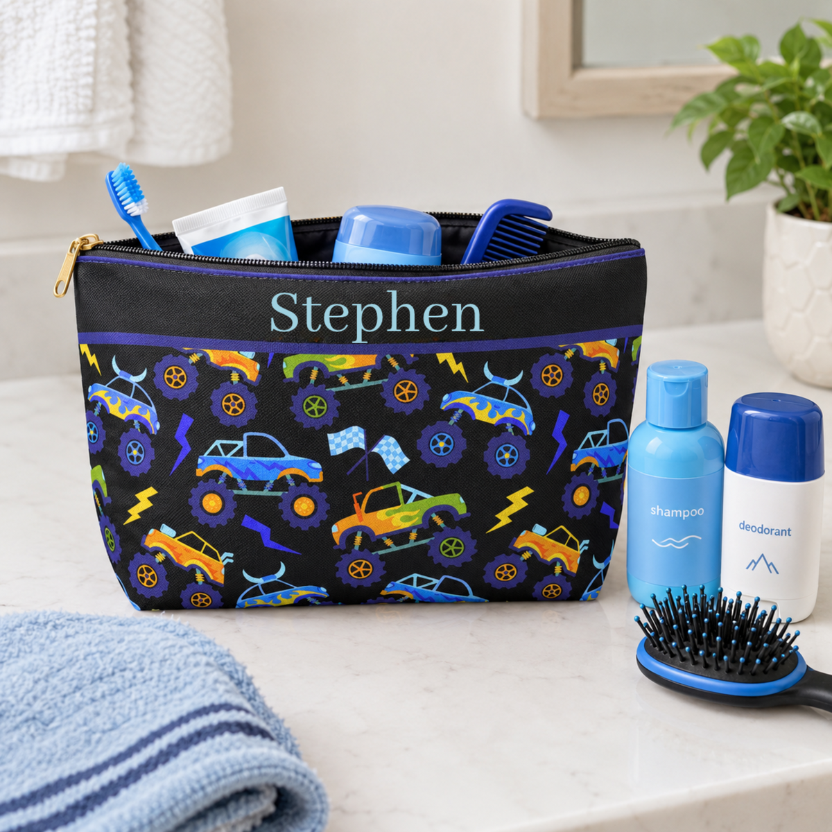 Personalized monster truck toiletry bag for boys shown with children's travel toiletries including a toothbrush, toothpaste, hairbrush and other personal care essentials. The black zipper pouch features colorful monster trucks, oversized wheels, lightning bolts and racing flags in bright blue, purple, yellow, orange and green, making it a fun kids travel bag for vacations, camp and sleepovers.