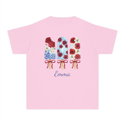 A light pink short sleeve t-shirt with a graphic of three decorated popsicles and the name 'Emma' printed below in blue cursive, displayed on a solid white background.