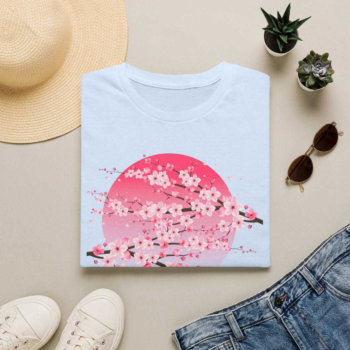 Folded light blue women's cherry blossom t shirt with pink sakura floral graphic, Japanese aesthetic design, styled with a straw sun hat, sunglasses, white sneakers and jeans