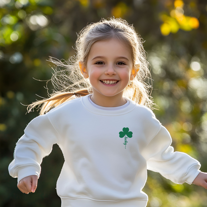 Young girl wearing a white youth crewneck sweatshirt featuring lucky shamrock embroidery with a green four leaf clover and the stem spelling “Lucky” in elegant script stitching. This festive kids St Patrick’s Day sweatshirt is made on a Gildan 18000B youth crewneck and is perfect for school celebrations, St Patrick’s Day parades, festive March outfits, and matching family St Patrick’s Day sweatshirts. 