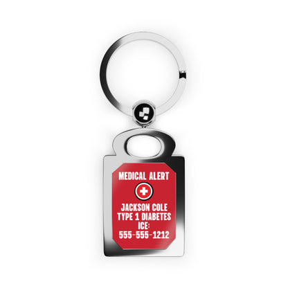 A medical alert keychain with a polished silver metal split ring and a rectangular tag featuring a red background with white text and a white cross symbol. The tag reads 'MEDICAL ALERT', 'JACKSON COLE TYPE 1 DIABETES', 'ICE:', and '555-555-1212'.