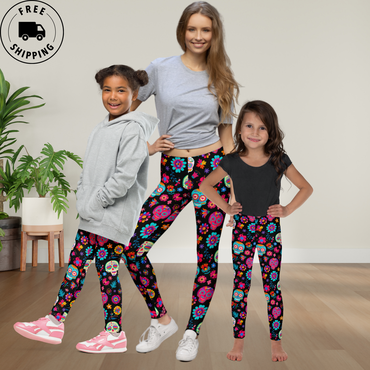 Mom and two daughters wearing matching Día de los Muertos leggings featuring colorful sugar skulls, flowers, and festive patterns on a black background. The coordinated leggings create a fun Mommy and Me look for celebrating Day of the Dead together, with girls sizes 2T through 20 and matching women’s sizes available.