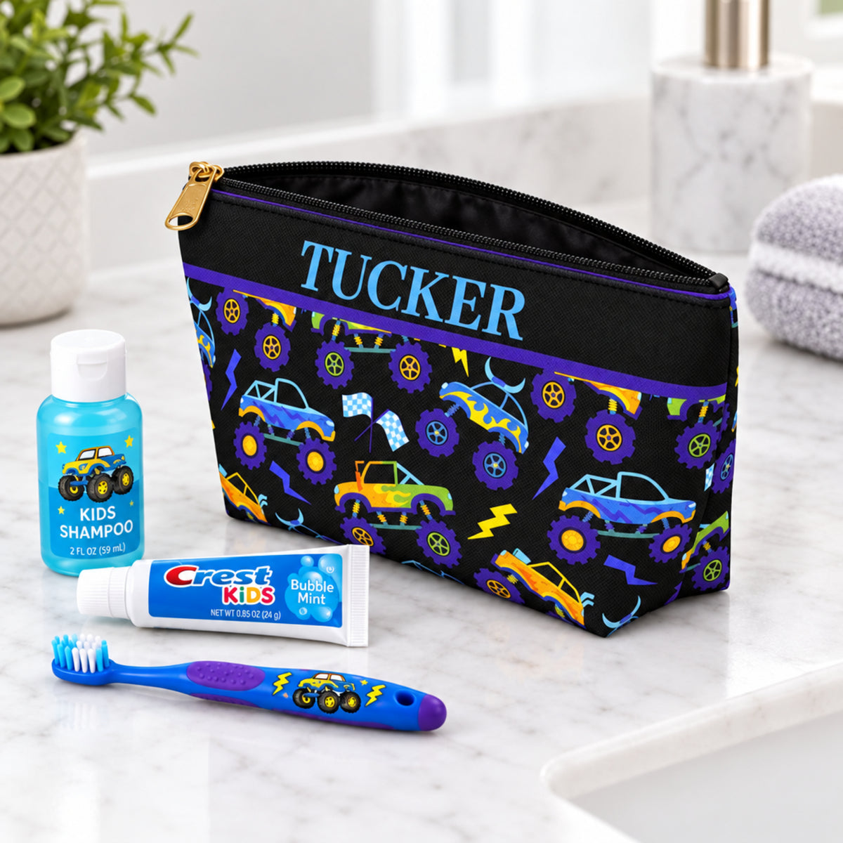 Personalized monster truck toiletry bag displayed as a birthday gift for a boy, with colorful monster trucks, oversized wheels, lightning bolts and checkered racing flags on a black pouch. The personalized travel bag has a zipper closure and fun racing inspired design, making it a useful gift for boys who love monster trucks, travel, sleepovers, summer camp and family vacations.