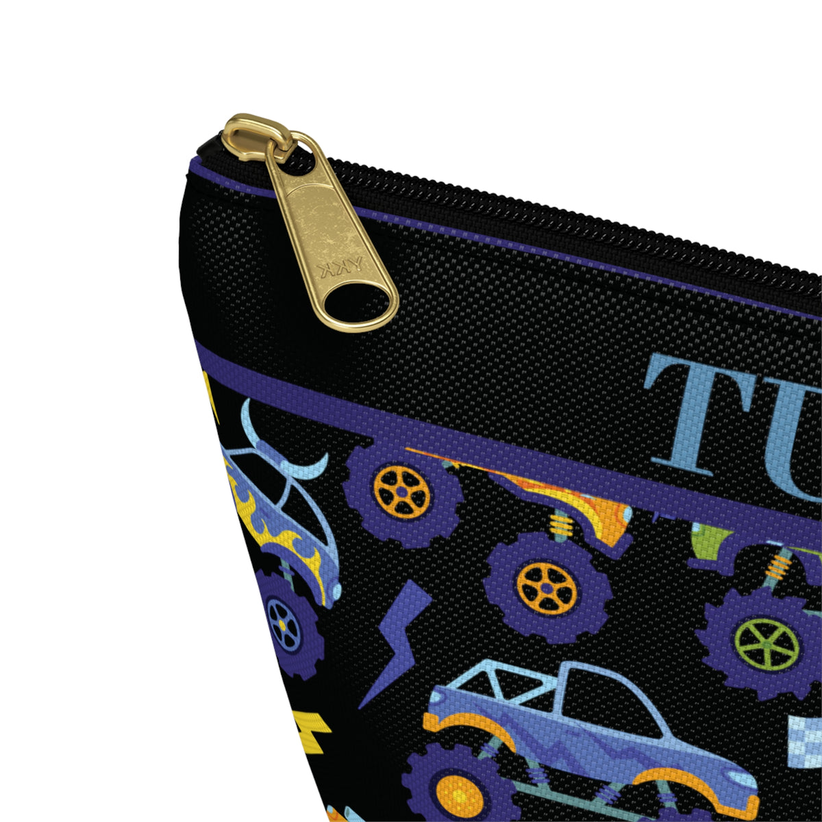 Close up of a personalized boys toiletry bag showing the name Tucker in orange lettering above a colorful monster truck pattern. The black pouch has a gold tone zipper pull, purple trim and detailed racing inspired graphics including monster trucks, oversized tires, lightning bolts and checkered flags. A fun personalized travel pouch for boys who love trucks and racing.