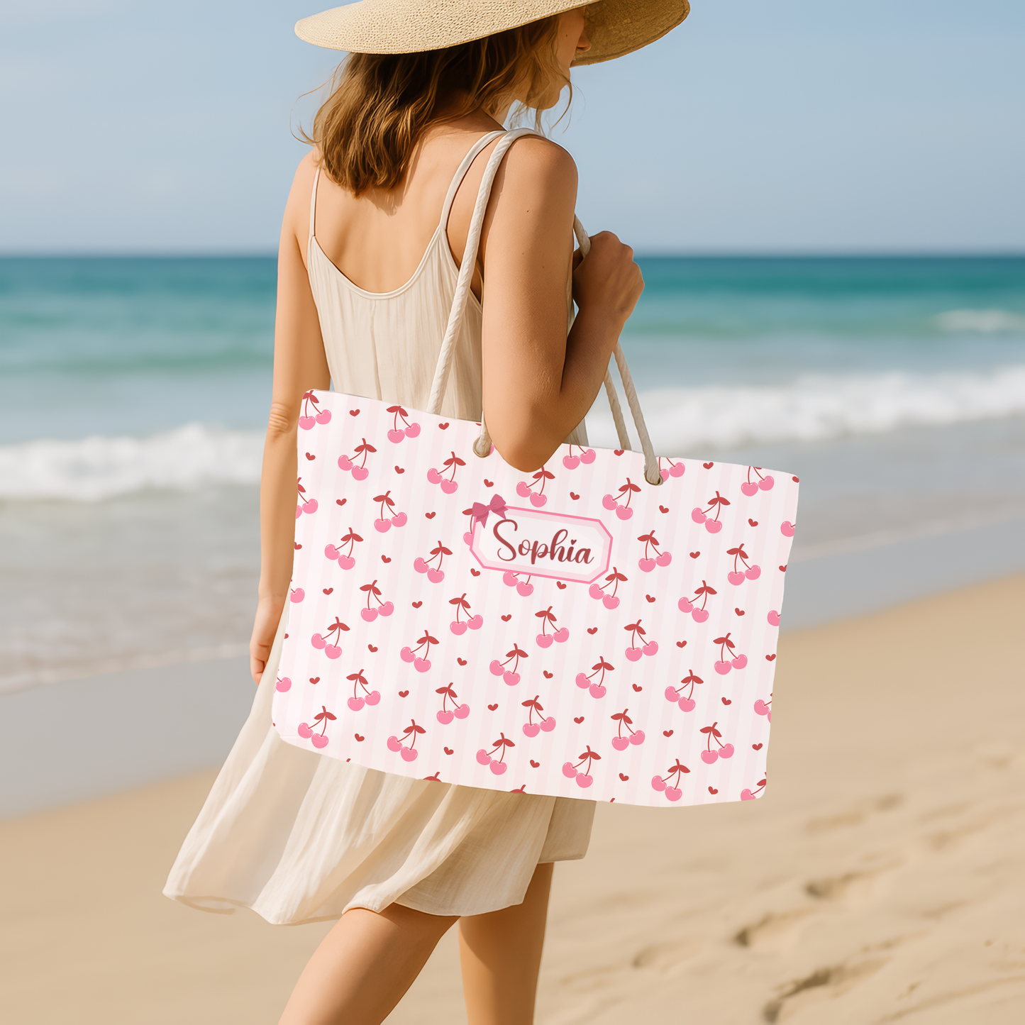 A woman carries the personalized coquette cherry weekender bag while walking along the beach, showcasing its stylish design in a real life travel setting. The oversized tote features a charming cherry print and custom name personalization, making it a beautiful companion for vacations, weekend getaways, cruises, and seaside adventures. Spacious enough for towels, a change of clothes, sunscreen, and travel essentials, this custom bag blends function with a soft girl aesthetic and makes a thoughtful gift for 