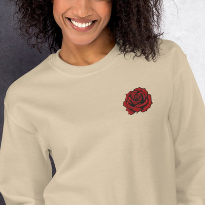 Front view of a sand colored women's crewneck sweatshirt featuring a red embroidered rose on the chest. The warm neutral shade and delicate floral stitching create a versatile look that pairs well with denim, casual trousers, and leggings. This embroidered rose sweatshirt is a thoughtful gift for women who enjoy understated floral clothing and classic botanical designs.