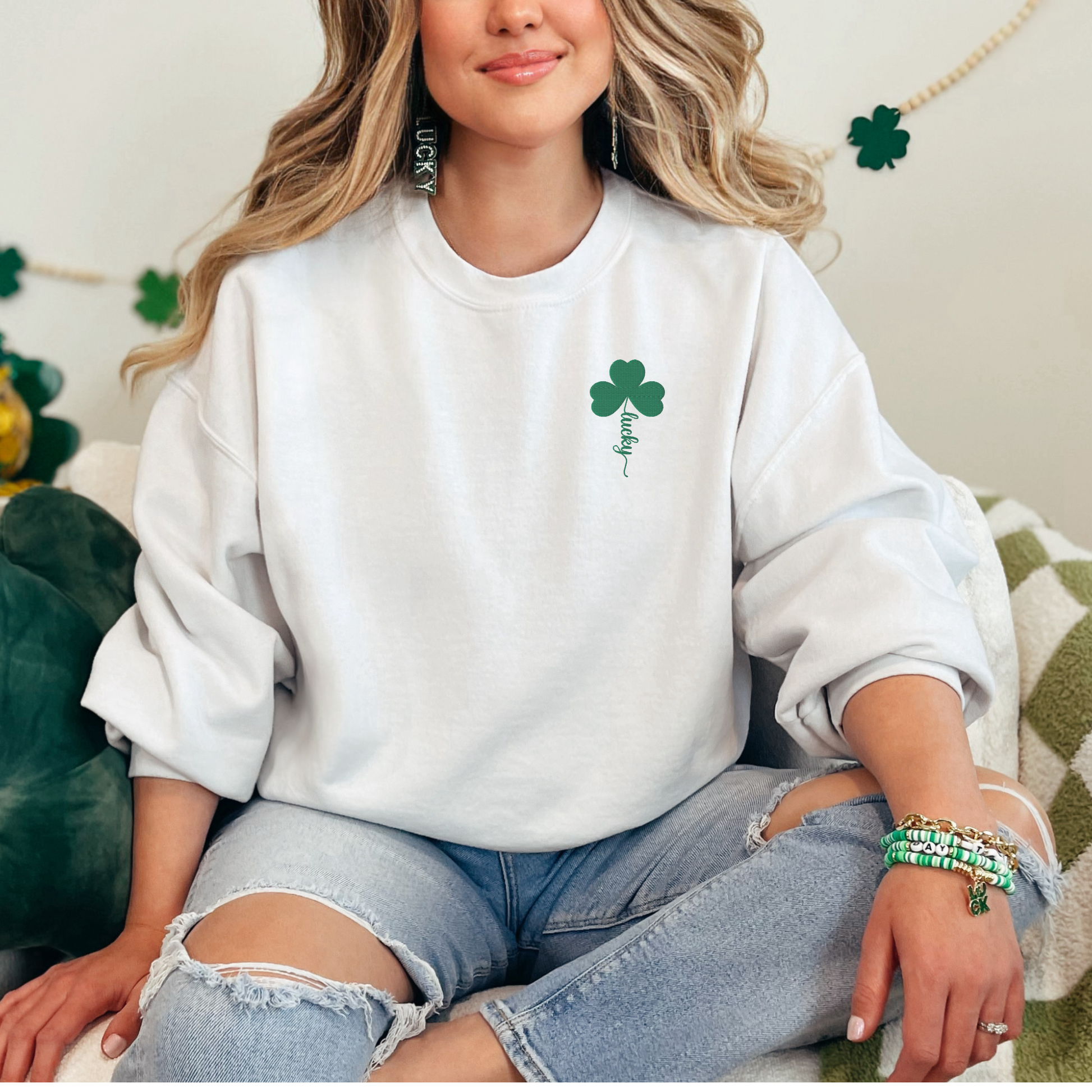 Front view of the Lucky embroidered St. Patrick's Day sweatshirt featuring a white crewneck pullover with green four leaf clover embroidery and script lettering on the stem.