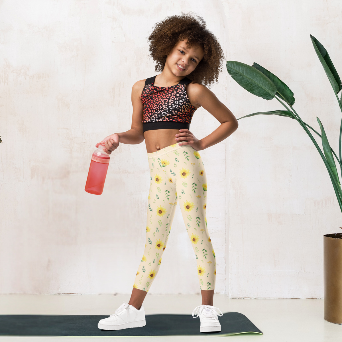 A pair of girls floral leggings covered with yellow sunflowers, green foliage and delicate botanical flowers against a soft cream background. The wildflower inspired design creates a cheerful garden look that works for toddlers, kids, tweens and teens. The full length high rise style is easy to pair with simple tops, sweatshirts, cardigans and sneakers for school, playtime, family outings, vacations and everyday wear.