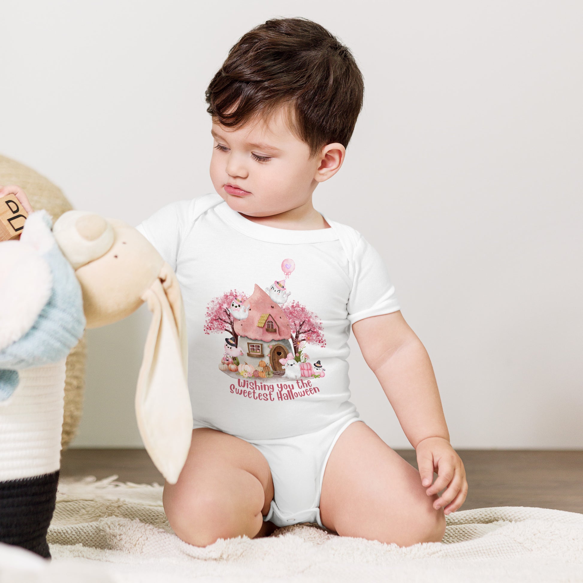 Image: Sweet and spooky come together in this pink Halloween baby onesie, with charming illustrations of friendly ghosts and pumpkins in a soft fairy garden setting. The baby bodysuit is made from cozy fabric with quick change snaps, ideal for baby girl’s first Halloween celebration, fall birthdays, and themed baby shower gifts, by jaecrece.