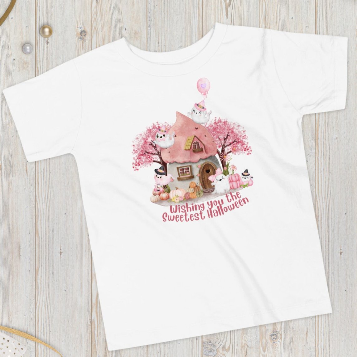 Pink toddler tshirt with a storybook cottage, pink trees, pink pumpkins and five sweet ghosts. The text reads Wishing you the sweetest halloween, by jaecrece