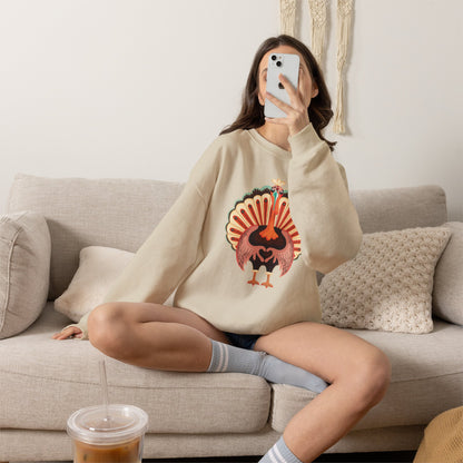A woman takes a mirror selfie while sitting on a beige couch, wearing a cream-colored sweatshirt with a colorful turkey graphic on the front. She is wearing gray striped socks and has an iced coffee in the foreground. Thanksgiving turkey sweatshirt with adorable colorful turkey making a heart shape with its wings, a cute family matching outfit for Thanksgiving dinner and fall gatherings