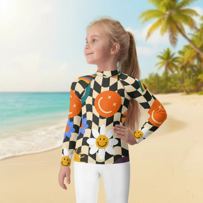 Tween girl on vacation wearing a retro wavy checkerboard girls rash guard with colorful smiley faces, rainbows, daisies, stars, and swirls. Long sleeve UPF 50+ swim shirt available in sizes 2T–20 with coordinating girls swimsuits, women's swimsuits, and men's swim trunks.