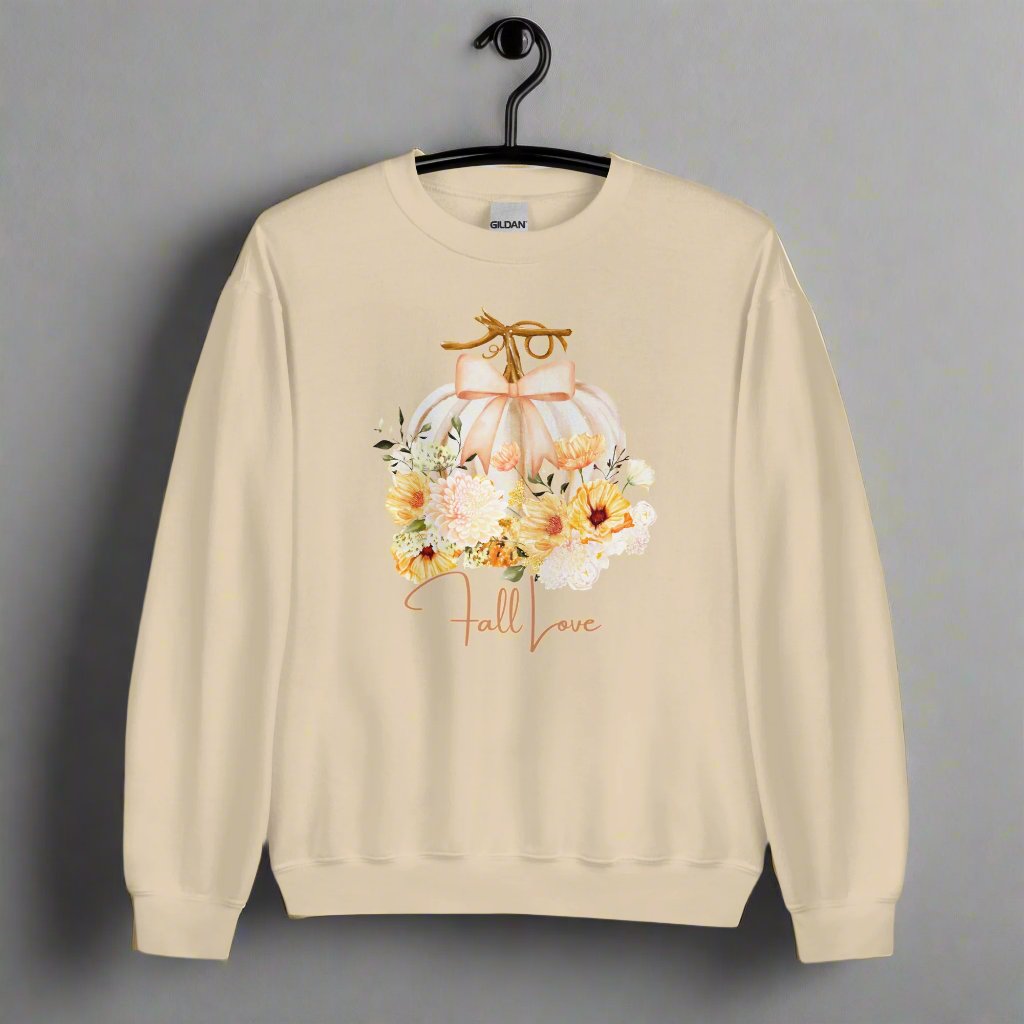 Fall Love Ladies Sweatshirt, this is a Sand colored Gildan Sweatshirt, with a graphic of a white pumpkin with a peach ribbon. The pumpkin is surrounded by a garland of fall leaves and flowers, with the text- Fall Love, by jaecrece