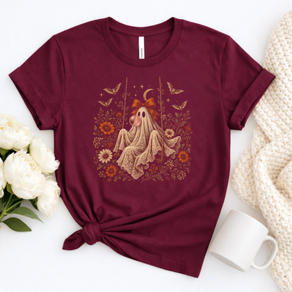Maroon girls Halloween T shirt shown in a flatlay featuring a whimsical vintage ghost blowing bubble gum, surrounded by orange flowers, botanical foliage, bats, stars, lace and a bow. A cute spooky season graphic tee for girls who love vintage Halloween artwork, fall fashion and playful ghost designs.