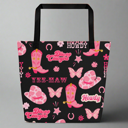 Image: Disco Cowgirl Tote Bag. This western glam canvas shoulder bag has a black background with a pink, white and pink pattern of butterflies, daisies, cowgirl hats and boots. The text on the bag reads Howdy, Yee-Haw and Disco Cowgirl. Great for weekend girls trips or bachelorette parties in Nashville, by jaecrece