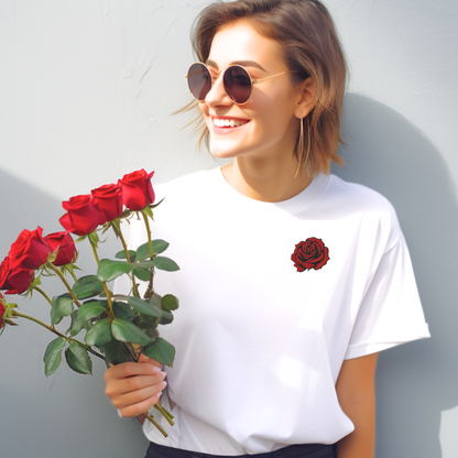 Woman wearing a white embroidered rose t shirt featuring a bold red rose floral embroidery centered on the chest. The soft cotton shirt is styled casually, highlighting the contrast between the crisp white fabric and the detailed rose stitching inspired by traditional tattoo art. The rose represents the June birth flower, symbolizing love and beauty, making this a meaningful gift for her birthday, anniversary, or everyday wear for women who love floral embroidery and romantic design.
