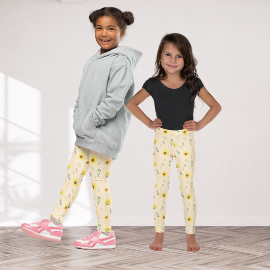 Close view of girls wildflower leggings showing the detailed floral pattern against a warm cream background. Yellow sunflowers are mixed with green leaves, leafy stems and smaller flowers to create a natural botanical meadow feeling. The soft stretchy fabric makes the leggings comfortable for everyday movement, while the cottagecore inspired design adds personality to spring and summer outfits, garden visits, family photos and casual days.