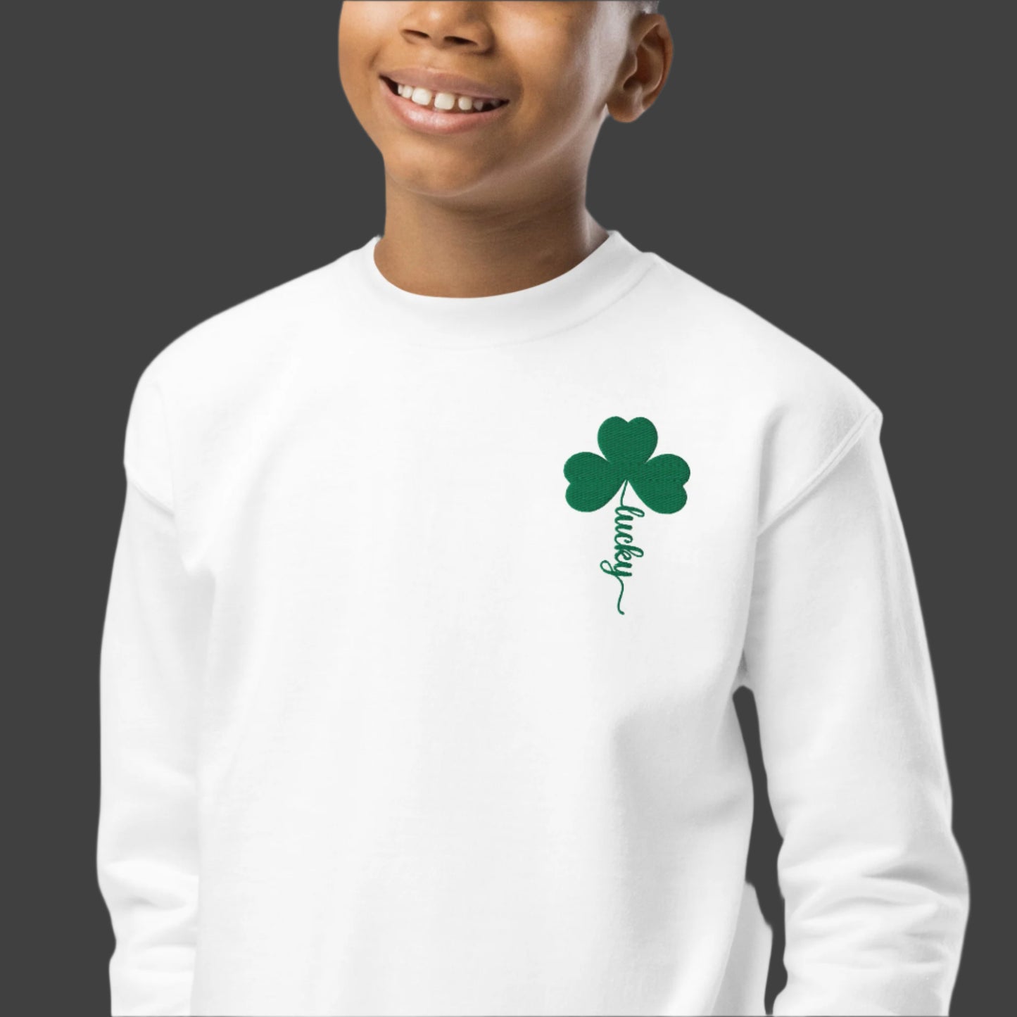 Image: St Patricks Day Emboidered Shamrock Lucky Sweatshirt. This white crewneck pullover has embroidered green four leaf clover, and stem of the  clover spells Lucky. Available in sizes for toddlers, girls, boys tweens, by jaecrece