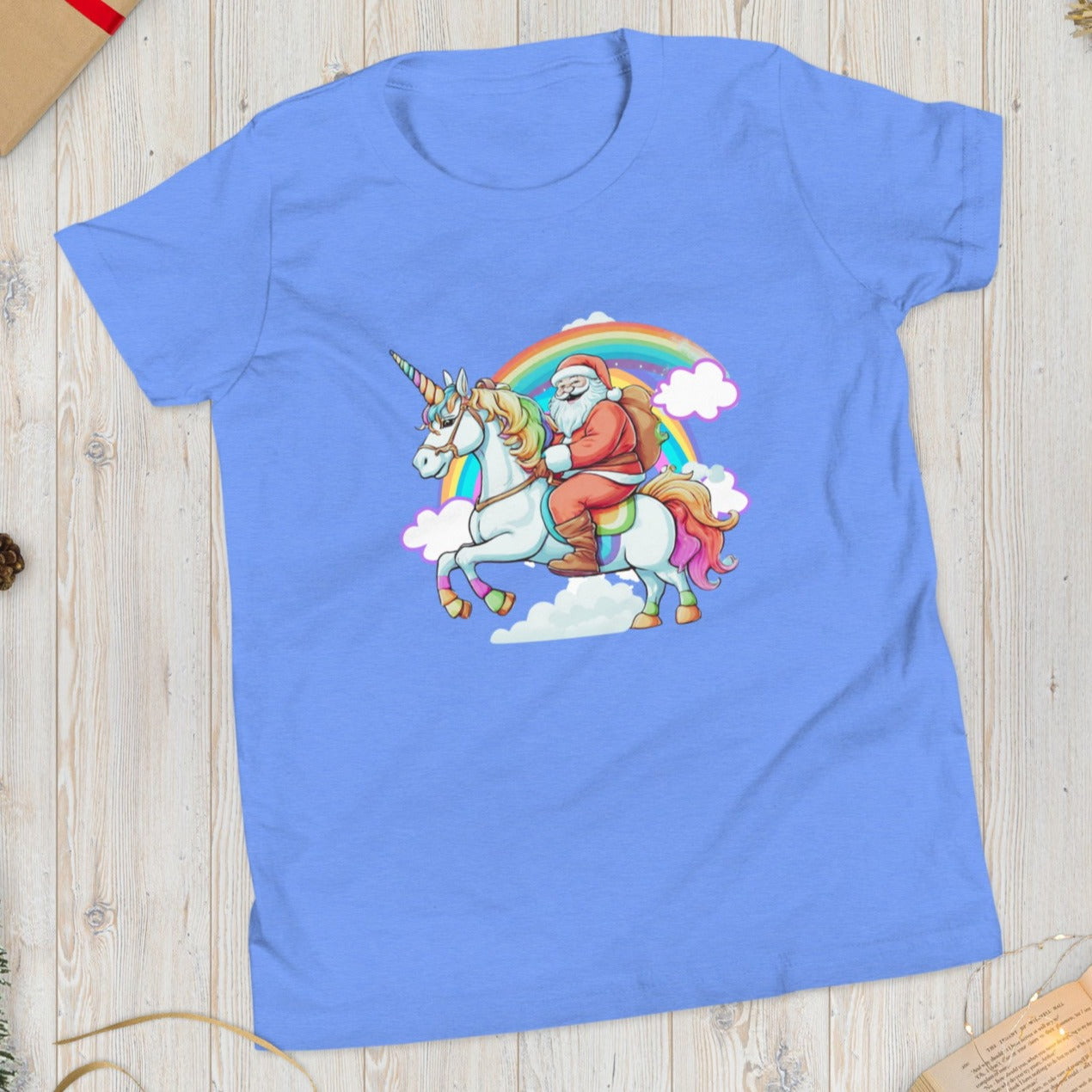 Alt Text: Blue short sleeve tshirt, featuring a whimsical scene of Santa riding on a unicorn over a rainbow with clouds